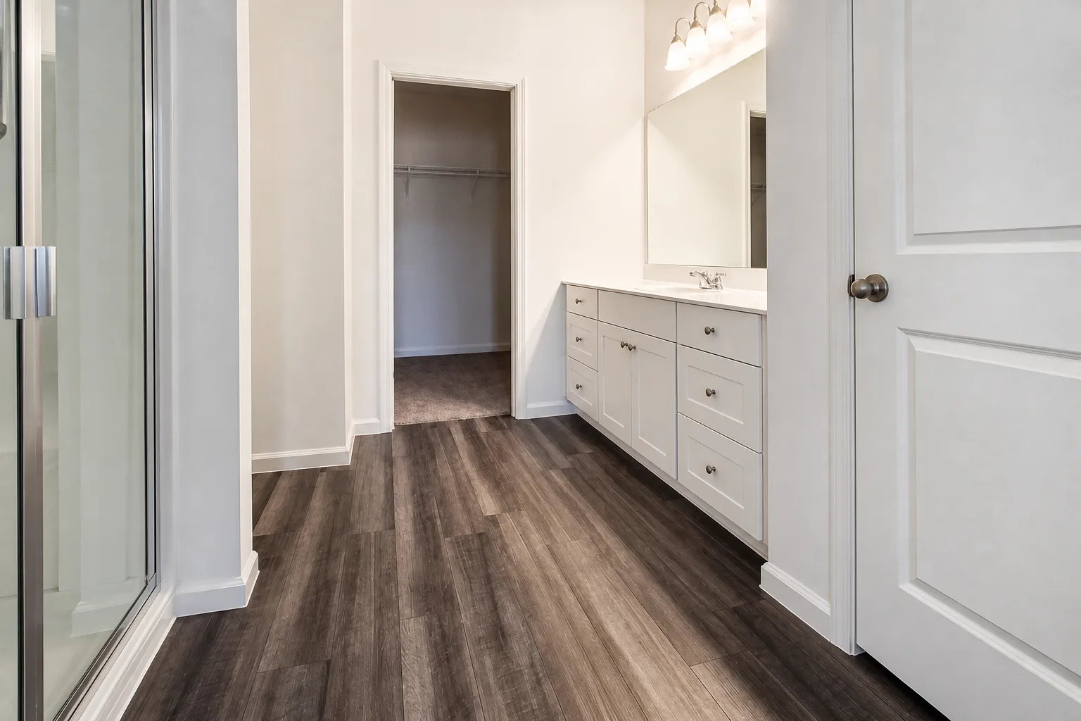 Wide-plank flooring leading to a primary vanity